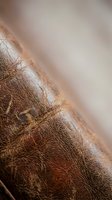 Close-up macro shot of brown leather texture with natural grain patterns and stitching details, showcasing rich material surface for luxury goods design.