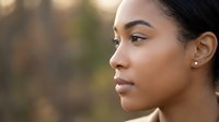 Young African American woman in profile with natural makeup and earrings looking thoughtfully into distance with soft golden light and blurred background.