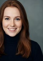 Young Caucasian woman with long brown hair smiling warmly in black turtleneck sweater against gray background for professional headshot photography.