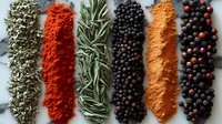 Colorful rows of aromatic spices and herbs including dried rosemary, paprika powder, black peppercorns, turmeric and mixed berries on dark surface. Food seasoning.