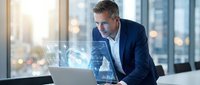 Professional businessman analyzing digital data analytics on laptop in modern office with holographic charts and graphs for business intelligence solutions.