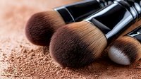 Professional makeup brushes with scattered loose powder foundation on beige background, close-up view showing soft bristles and black handles for cosmetics and beauty industry.
