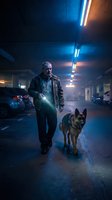 Senior Caucasian man with German Shepherd dog walking through underground parking garage at night with dramatic neon lighting and atmospheric fog.