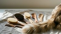 Assorted wooden brushes and combs arranged with long golden hair strands on neutral linen fabric for grooming, beauty care, and hair styling product marketing.