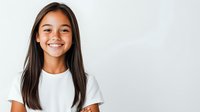 Young Asian woman with long dark hair wearing white t-shirt smiling brightly against light gray background, showing genuine happiness and confidence in casual studio portrait.