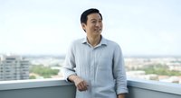 Asian male professional in light blue button-up shirt leaning against railing on high-rise balcony with cityscape view, looking away thoughtfully, suitable for business, corporate, and lifestyle content.