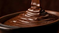 Melted chocolate drips from spoon into bowl of smooth, glossy chocolate sauce, creating rich, decadent dessert preparation for baking and confectionery projects.