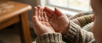Open cupped hands in prayer or receiving gesture wearing knitted sweater in warm natural light for spiritual and wellness concepts.