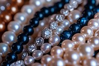 Elegant pearl necklaces with white, black, and pink pearls interwoven with sparkling crystal rhinestone elements in diagonal rows, macro jewelry photography.