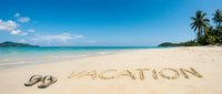 Vacation written on sandy tropical beach with flip flops, turquoise ocean, palm trees, and blue sky, evoking summer travel and holiday relaxation.
