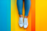 Female legs in blue skinny jeans and white sneakers standing on vibrant multicolored striped background. Modern minimal fashion composition for social media and advertising.