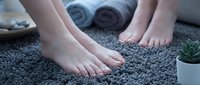 Woman bare feet on soft gray carpet in spa bathroom with towels and succulent plant creating relaxing wellness atmosphere for self-care routine.