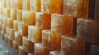 Stacked blocks of natural Himalayan salt with sunlight creating warm amber glow, showing crystalline texture and mineral patterns in rows. Wellness and spa concept.