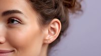 Close-up profile of young woman with natural makeup, glowing skin, and curly hair against purple background, showcasing ear with small stud earring.