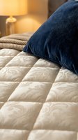 Cozy bedroom scene with navy blue pillow resting on cream quilted bedding, warm lamp glow, and striped cushion creating inviting sleep environment for home decor and lifestyle content.