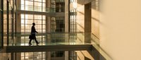 Professional businessman walking across modern office building bridge with dramatic lighting and geometric architecture creating sophisticated corporate atmosphere.