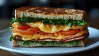 Grilled sandwich with layers of melted cheddar cheese, fresh tomato slices, crisp lettuce on toasted bread. Close-up view showing texture and ingredients.