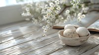 Rustic Easter composition with white eggs in ceramic bowl and spring flowers on wooden table in natural sunlight, perfect for seasonal holiday cards and decor inspiration.
