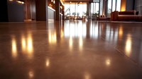 Polished concrete floor with warm light reflections in modern office lobby space, showing depth and perspective leading to blurred background seating area.