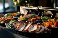 Sliced roasted meat with grilled vegetables on buffet serving trays, garnished with fresh herbs and colorful side dishes in restaurant catering setup.