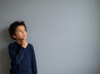 Young boy with curly dark hair and medium skin tone wearing navy blue long-sleeve shirt, looking upward thoughtfully against neutral gray wall background. Suitable for education, child development, and parenting concepts.