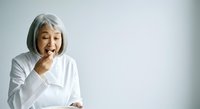 Senior woman with gray hair wearing white shirt laughing with hand near mouth against white background, expressing joy and happiness for lifestyle and wellness content.