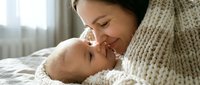 Loving mother in cozy knit sweater tenderly bonding with newborn baby in soft natural light. Intimate maternal moment capturing pure affection and care.