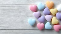 Colorful pastel heart-shaped candies scattered on white wooden background. Sweet romantic treats for Valentine's Day, love celebrations and holiday decorations.