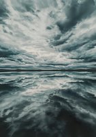 Dramatic stormy clouds reflected in still water creating mirror effect with moody teal tones. Atmospheric landscape showcases nature's symmetry and power.