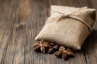 Aromatic star anise and coffee beans scattered near rustic burlap sack on weathered wooden background, creating cozy atmosphere for food and beverage designs.