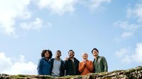 Group of five diverse adults standing outdoors against blue sky with clouds, wearing casual clothing in various colors, suitable for team, community, and lifestyle concepts.