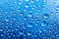 Pure water drops on blue surface create natural pattern with various sized spherical droplets showing surface tension and light reflection. Macro photography.
