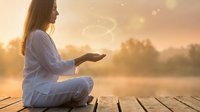 Young woman in white clothing practicing meditation on wooden dock during golden sunset with peaceful lake and forest background for wellness and mindfulness concepts.