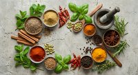 Colorful spices and herbs arranged in circular pattern on textured stone surface. Fresh basil, rosemary, cinnamon sticks, turmeric, paprika in wooden bowls.