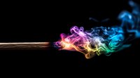 Burning match with colorful rainbow smoke trails against black background, dynamic motion capture of vibrant flowing smoke art in pink, yellow, and blue hues.