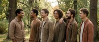 Group of six men standing together in forest setting wearing casual brown and neutral toned clothing, suitable for team, friendship, community, or ensemble cast concepts.