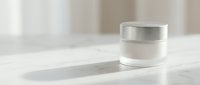 White cosmetic jar with silver cap on marble surface in soft natural light for skincare and beauty product packaging design.