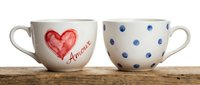 Pair of ceramic mugs with red heart and amore text on one, blue polka dots on reverse side, isolated on wooden surface for home decor and tableware design.