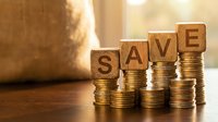 Wooden blocks spelling SAVE on stacks of golden coins with warm sunlight, representing financial savings and money management concepts.