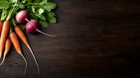 Fresh organic carrots and radishes with green leaves on dark wooden background, raw vegetables from garden. Food photography with copy space.
