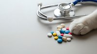 Medical stethoscope with colorful pills and capsules scattered on neutral background for healthcare and pharmaceutical concepts.