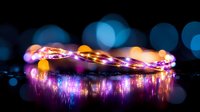 Glowing fairy lights create magical reflection on dark surface with purple and orange bokeh effects, romantic ambient lighting for festive decoration.