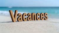 Wooden letters spelling "Vacances" on sandy beach with turquoise ocean and waves in background, summer holiday concept for travel design.