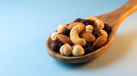 Mixed nuts and dried fruits in wooden spoon on blue background. Healthy snacking, trail mix with almonds, cashews, hazelnuts and raisins for nutrition.