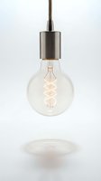 Vintage Edison bulb with warm filament glow suspended from braided cord and brushed metal fixture against white background, isolated for interior design and lighting projects.