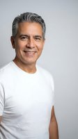 Confident mature Hispanic man with gray hair smiling warmly in white t-shirt against neutral background for professional headshot and lifestyle content.