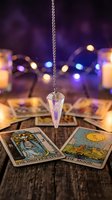Crystal pendulum hanging over tarot cards with mystical purple bokeh lights creating spiritual divination atmosphere for fortune telling sessions.