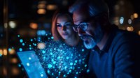 Senior Caucasian man with glasses and young woman looking at glowing tablet with magical blue particles effect, digital transformation concept in dark room.