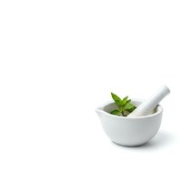 White ceramic mortar and pestle with fresh green herbs isolated on white background for natural medicine and cooking applications.