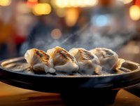 Steaming hot Asian dumplings on black plate with golden bokeh background, close-up view of grilled gyoza with rising smoke, atmospheric restaurant setting.